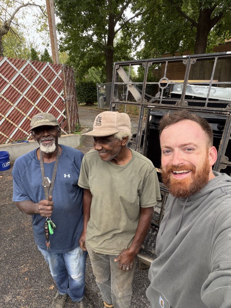 Two neighbors and a volunteer smiling together beside a truck full of scrap