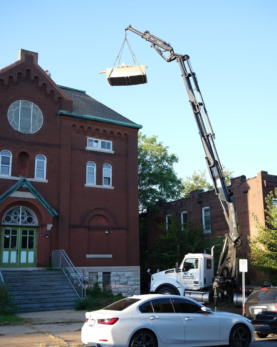 A crane lifting roofing materials onto the old brick school building