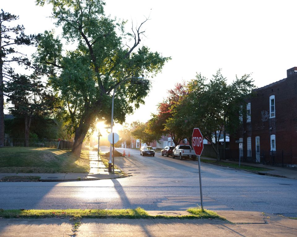 A Dutchtown street at sunset, brick two-flats and trees, the sun low at the end of the block